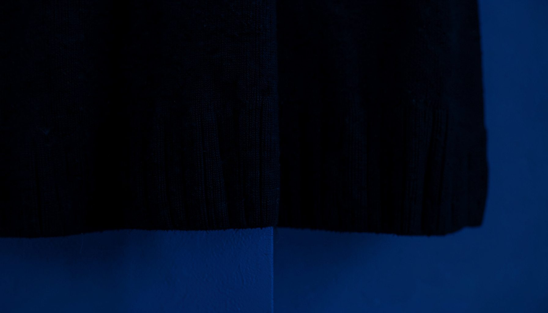 Close-up of dark fabric with ribbed hem texture, minimal and moody