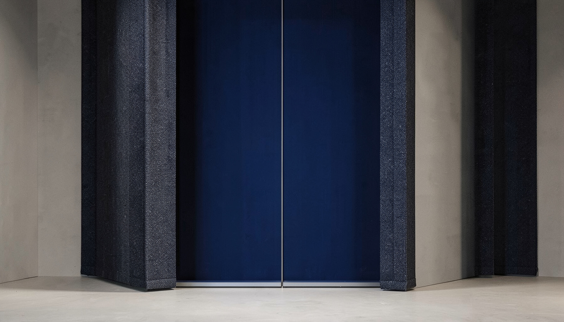 Clean architectural photograph with strong symmetry, dark navy and charcoal fabric textures against a muted neutral background