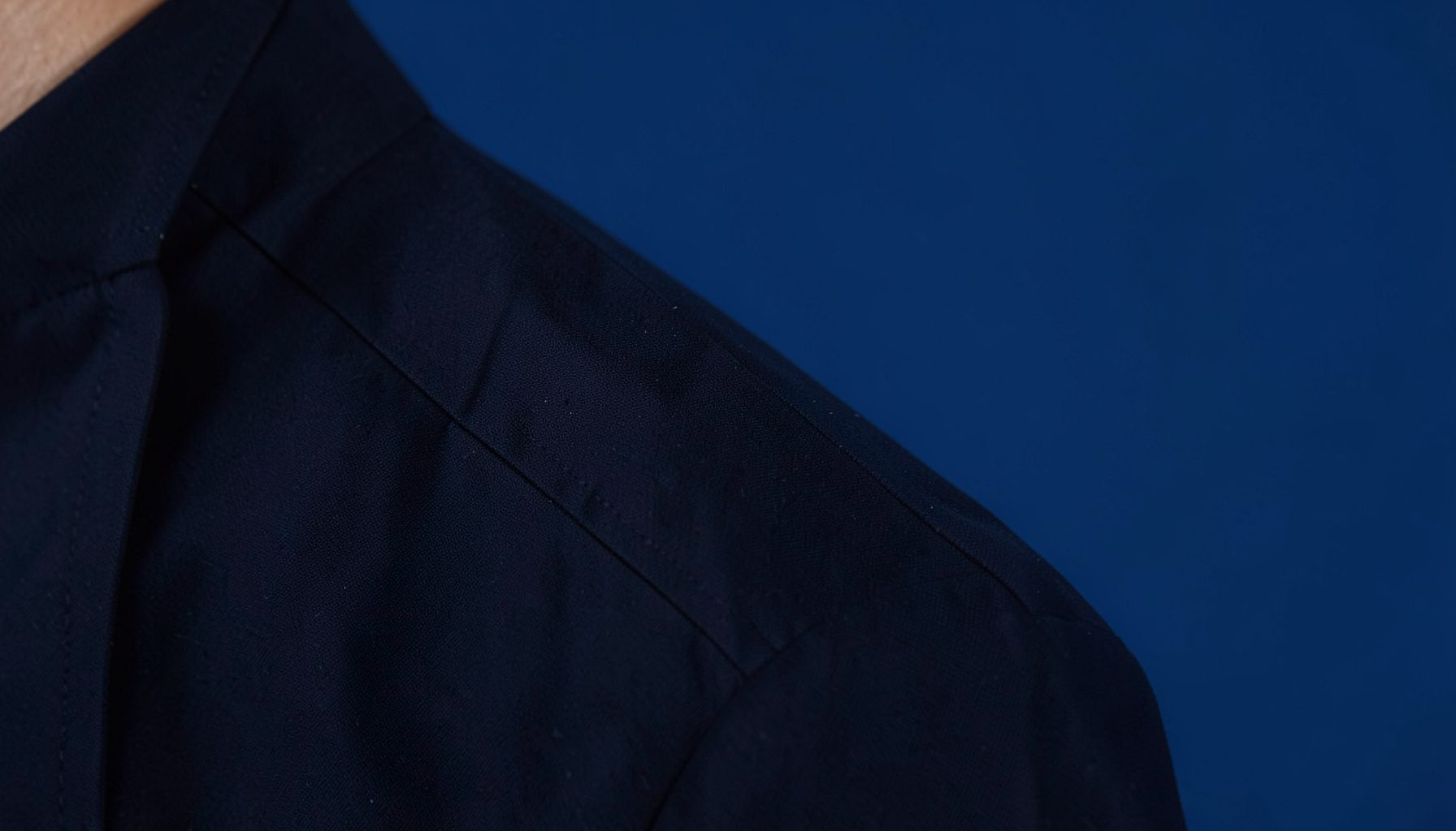 Close-up of dark navy jacket collar and shoulder seam, subtle texture, clean tailoring