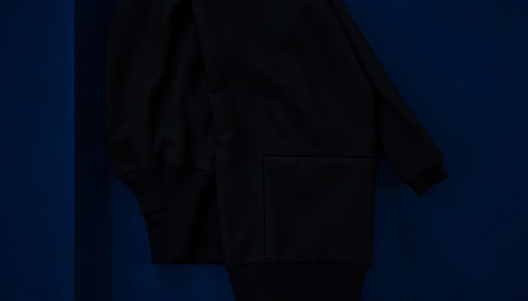 Dark folded jacket with ribbed cuff detail, deep black fabric, minimal and moody