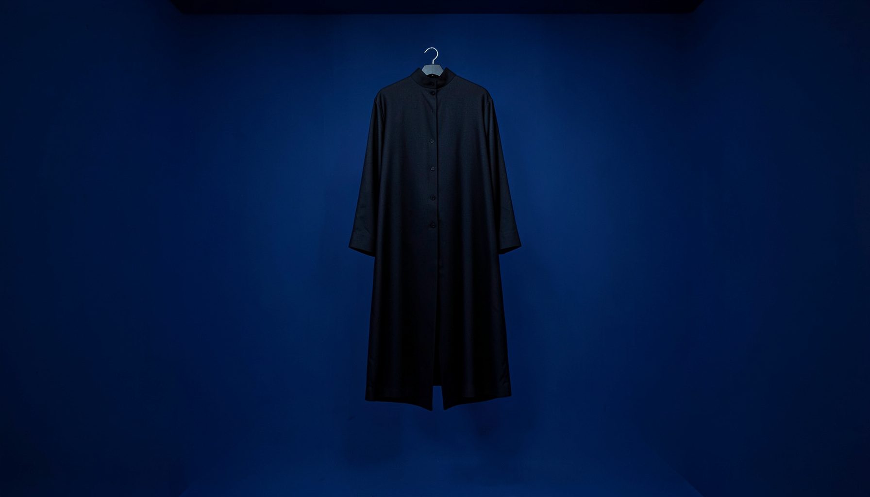 Clean architectural photograph of a dark garment hanging with strong symmetry, deep navy and black tones, gallery-like presentation